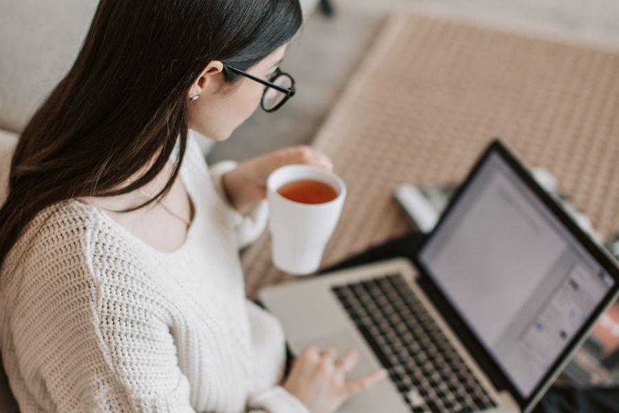 chica con un te en la mano mirando portátil